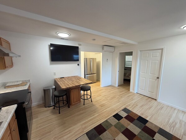 A modern kitchen with a wooden countertop, two bar stools, a TV mounted above the counter, and a refrigerator in the background. - Completely Updated Darling Home (Milwaukie)