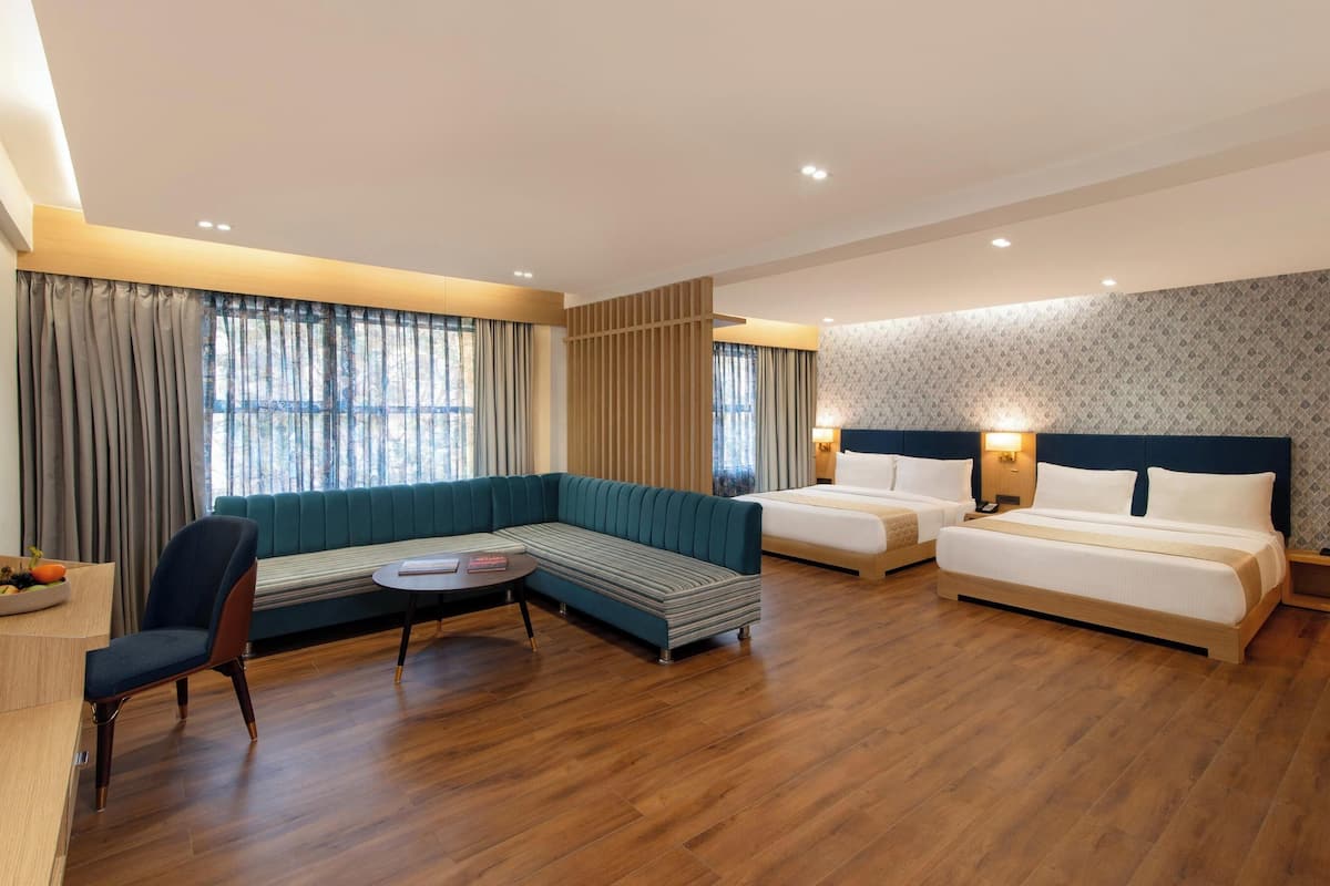 A modern hotel room with a sofa, two single beds, a small table, and a chair.