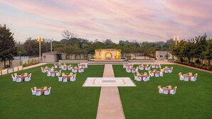 An outdoor wedding venue with a central stage, rows of tables and chairs, and a well-maintained lawn. - Amber-A Unit of Sayaji Hotels (Bhopal)