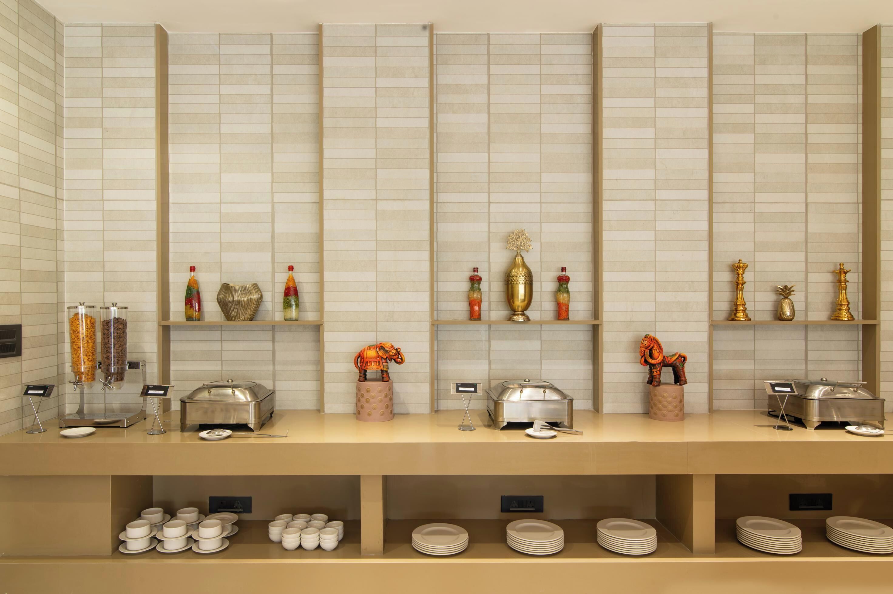A buffet setup with various food dispensers, serving dishes, and decorative items on shelves.