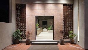 A modern entrance with a stone facade, potted plants, and a reception area visible through a wooden screen. - Amber-A Unit of Sayaji Hotels (Bhopal)