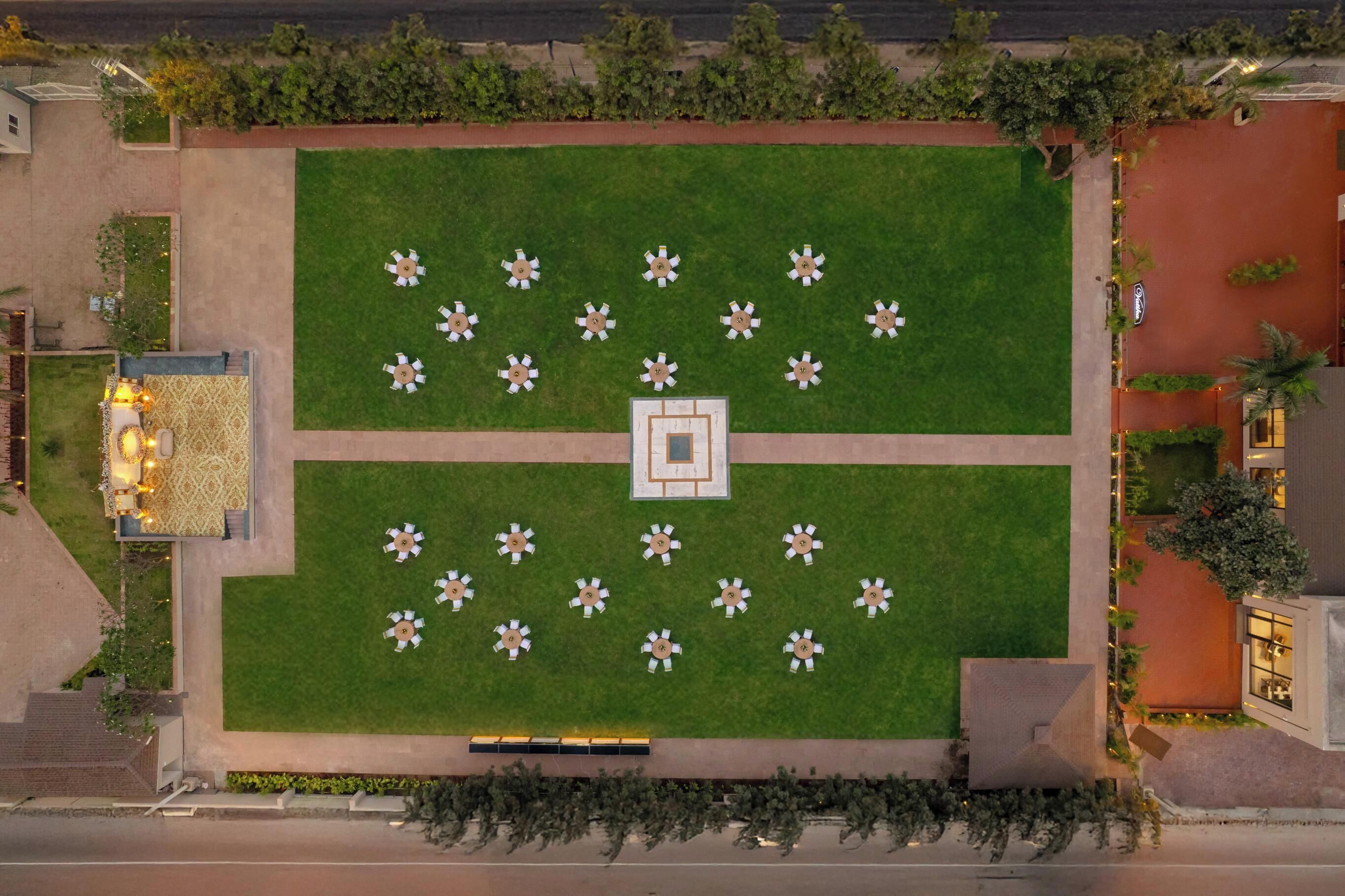 An aerial view of a hotel courtyard with a central square, surrounded by evenly spaced tables and chairs, and a patterned seating area to the left.