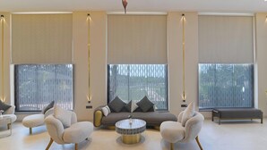 A modern living room with a sofa, two armchairs, a coffee table, and large windows with blinds. - Amber-A Unit of Sayaji Hotels (Bhopal)