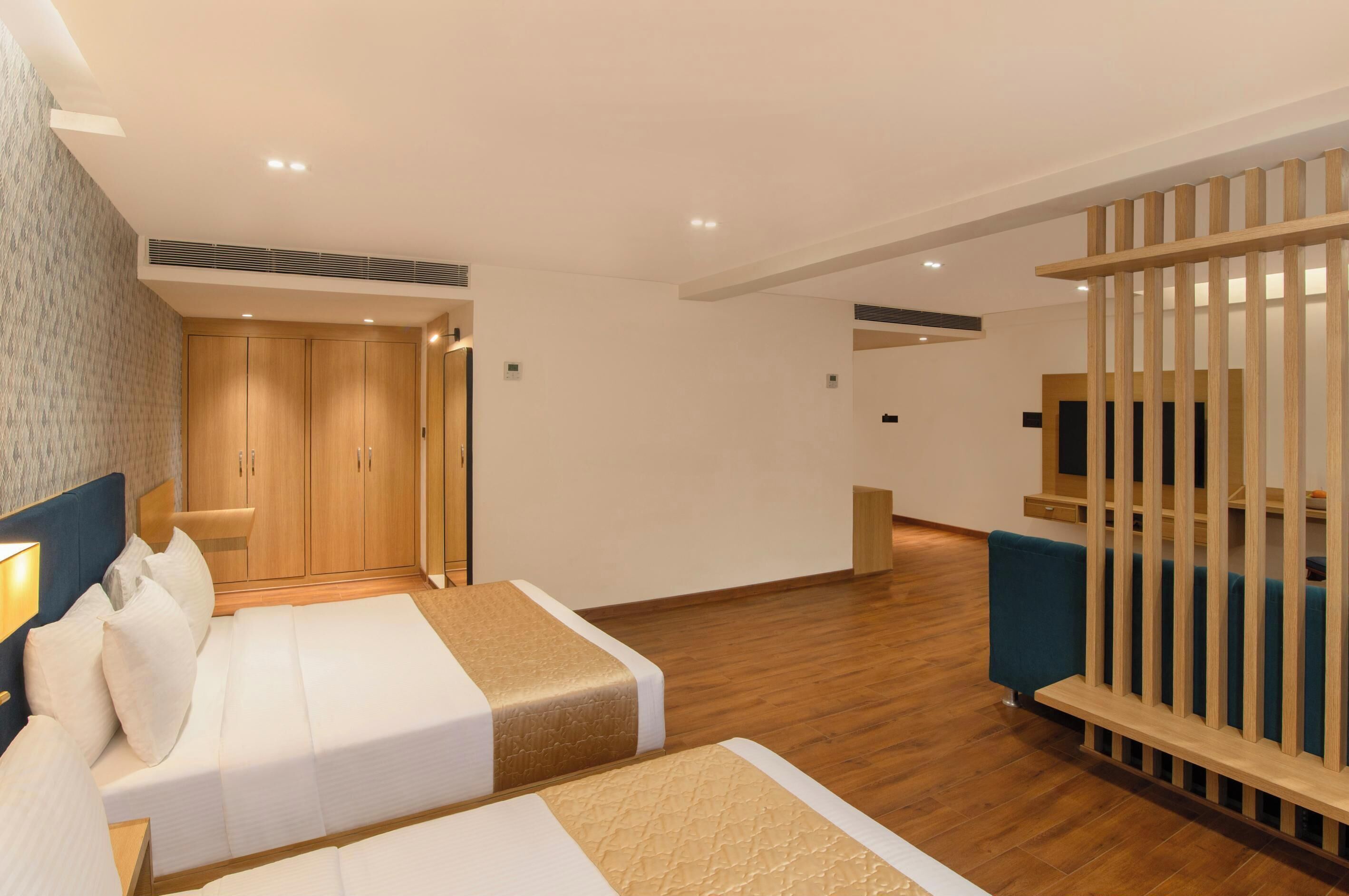 A modern hotel room with a large bed, a wardrobe, and a seating area with a wooden partition.
