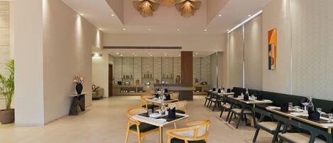 A modern restaurant with wooden chairs and tables, a central dining area, and a kitchen in the background.