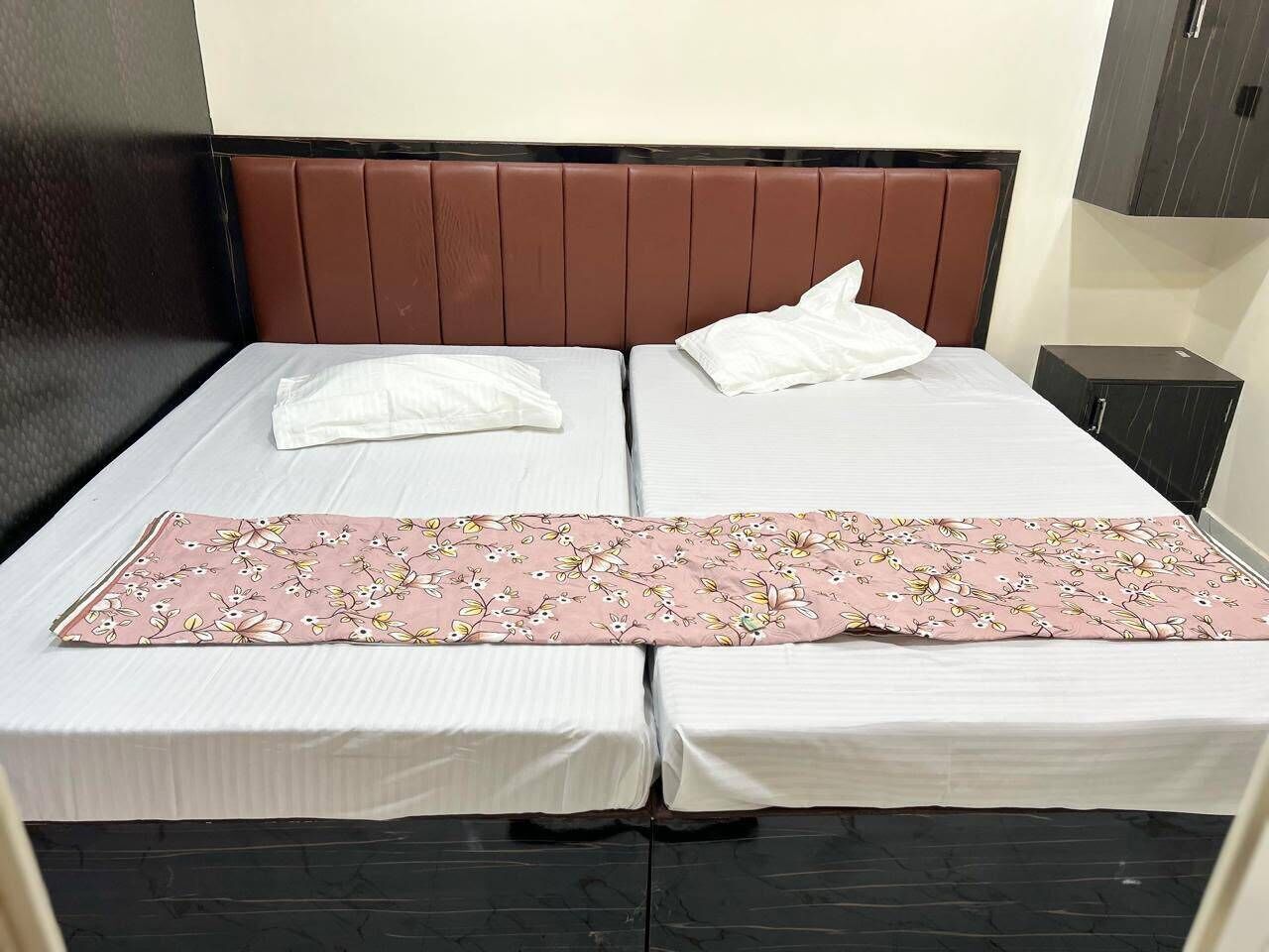 A double bed with a brown headboard, white bedding, and a pink floral bedspread.
