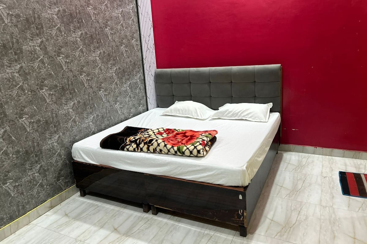 Un lit avec une tête de lit rembourrée de couleur grise, une literie blanche et un plaid à motifs floraux.
