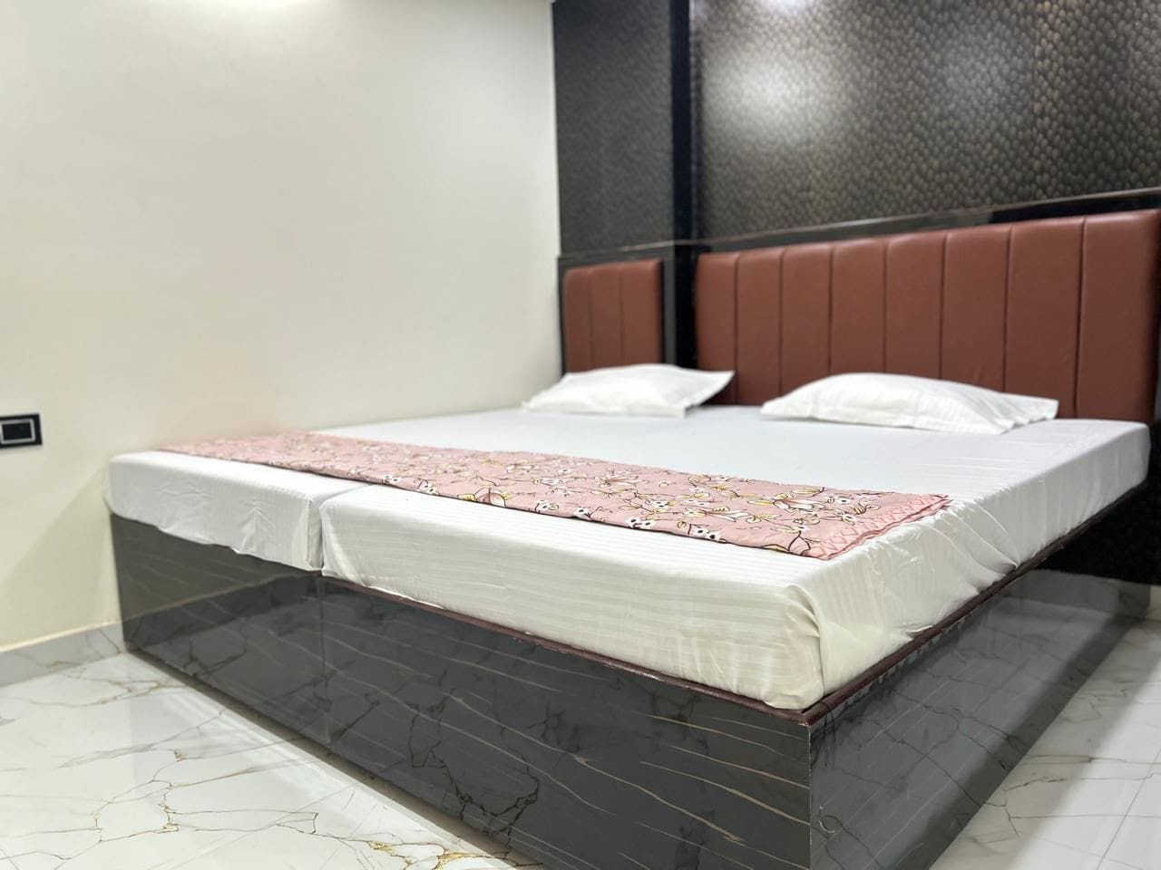 A bed with a white mattress and a pink blanket, a brown headboard, and a marble-patterned floor.