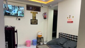 A room with a sofa, a pool table, a television displaying multiple camera feeds, a fire extinguisher, and a sign indicating checkout time. - New Jay Radhe Krishan Residency (Varanasi)