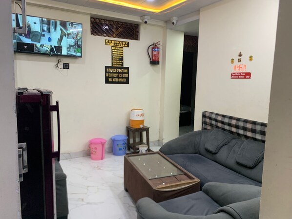 Una habitación con sofá, mesa de billar, televisor que muestra múltiples cámaras de seguridad, extintor de incendios y un cartel que indica la hora de salida.