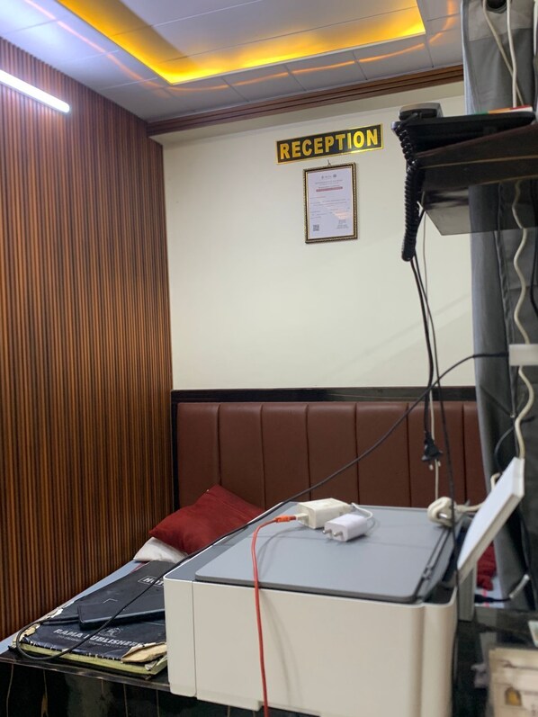 A reception area with a sign labeled 'RECEPTION' on the wall, a bed with a red pillow, and a medical device on a table. - New Jay Radhe Krishan Residency (Varanasi)
