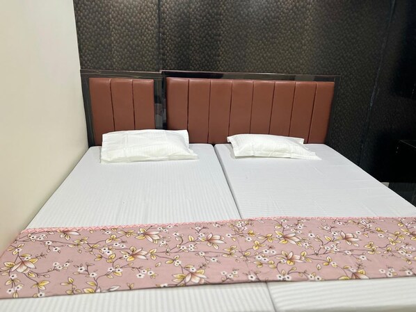 A double bed with a floral bedspread and two pillows, a brown headboard, and a textured wall behind. - New Jay Radhe Krishan Residency (Varanasi)