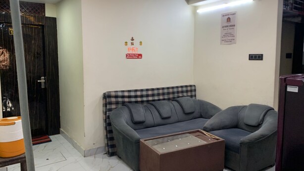 A room with a checkered sofa, a brown ottoman, and a wall-mounted sign indicating water quality. - New Jay Radhe Krishan Residency (Varanasi)