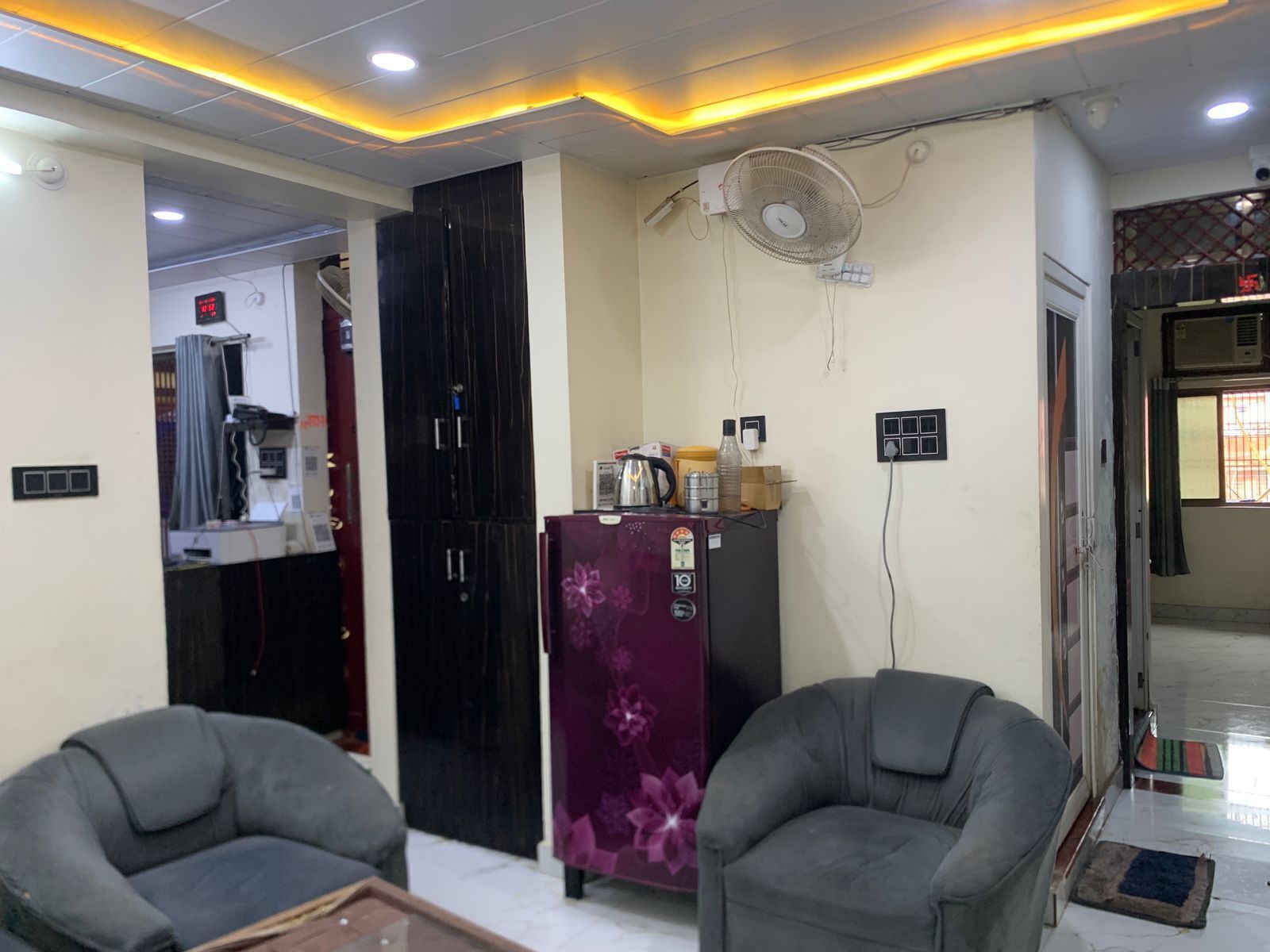 A living room with two grey armchairs, a purple refrigerator, and a ceiling fan.