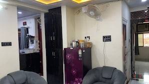 A living room with two grey armchairs, a purple refrigerator, and a ceiling fan. - New Jay Radhe Krishan Residency (Varanasi)