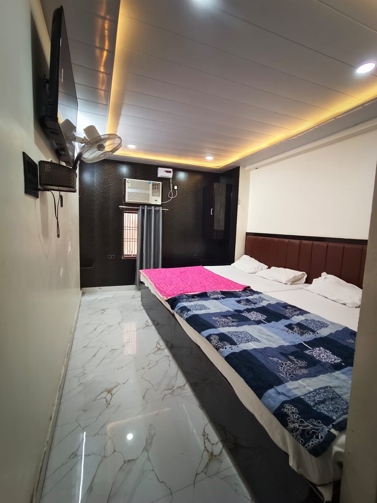 Un dormitorio con cama, televisor de pantalla plana montado en la pared, aire acondicionado y ventilador de techo.
