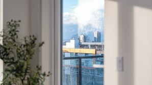 Quarto com uma janela grande, uma planta em vaso e vista para edifícios.
