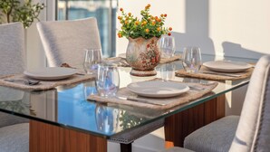 Uma sala de jantar com mesa de vidro, quatro cadeiras e um vaso com flores.
