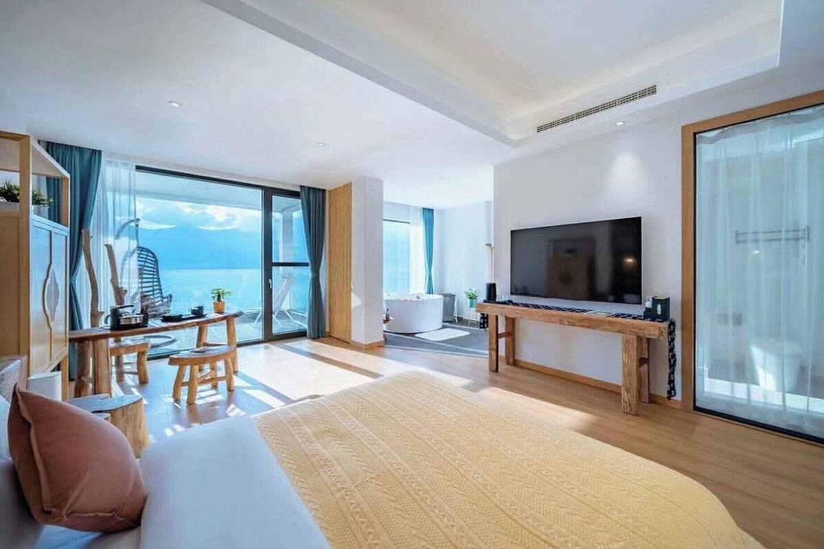 Un hotel moderno con una cama grande, televisión, balcón con vistas al mar y zona de comedor.
