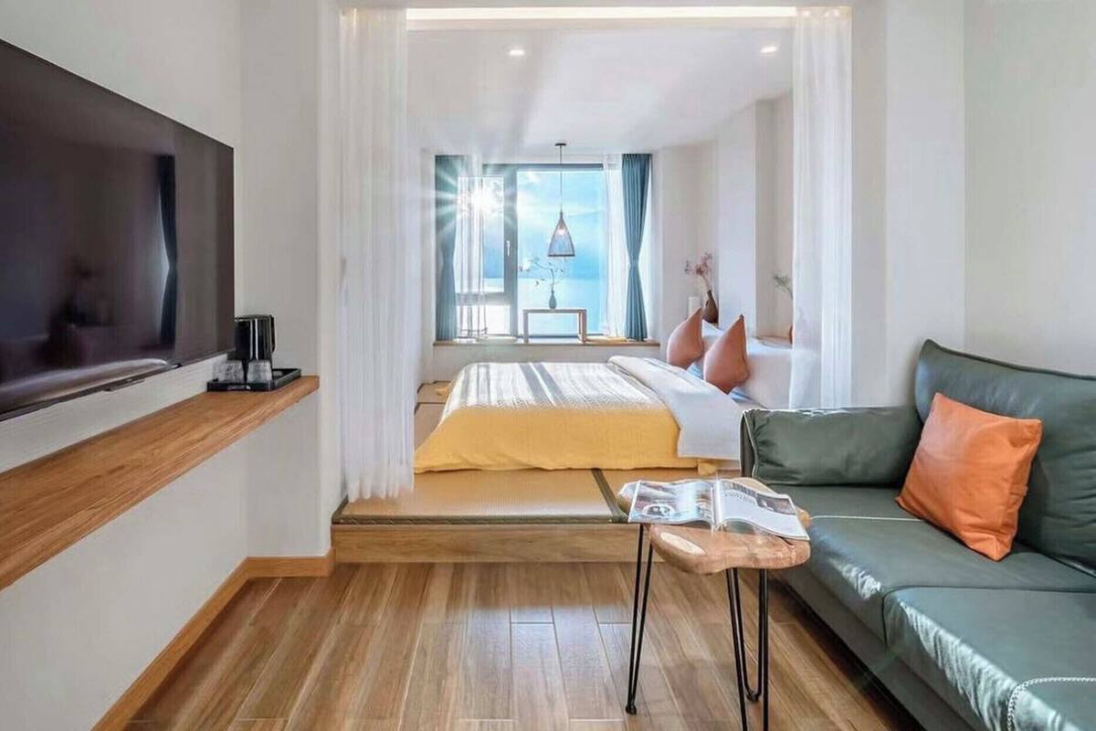 Habitación de hotel moderna con cama, sofá, televisor y ventana con vista al mar.