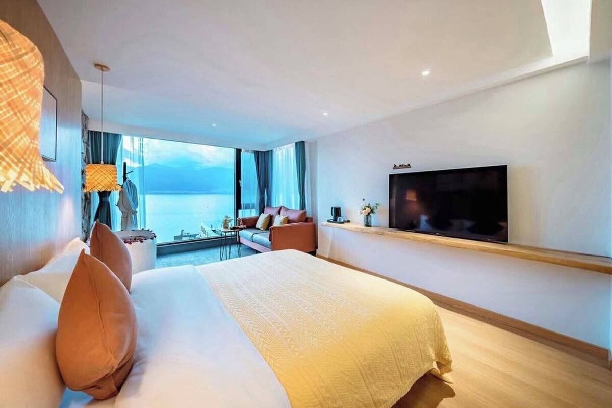 Una habitación de hotel moderna con una cama grande, un televisor de pantalla plana, un balcón con vistas al mar y una zona de comedor.