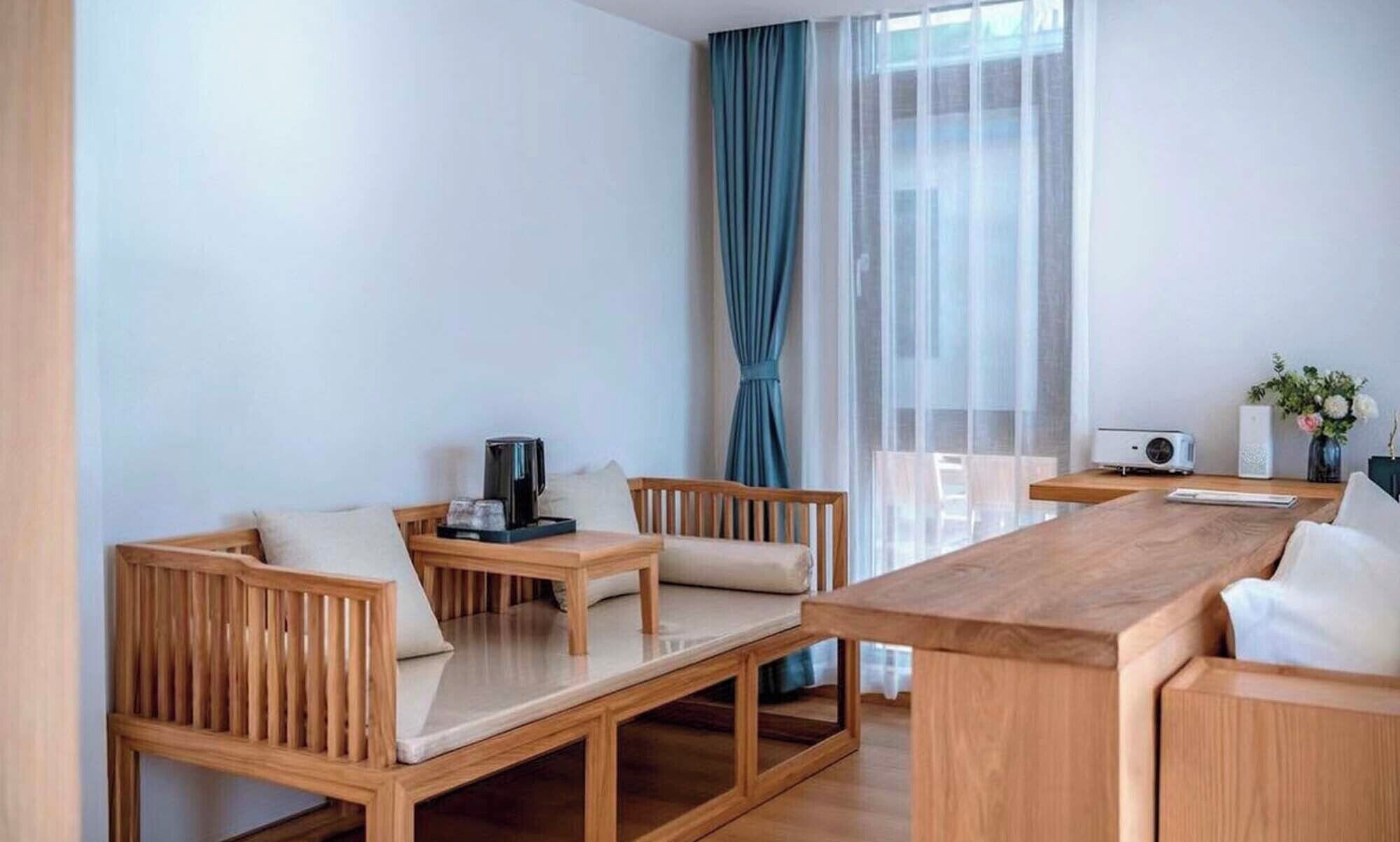 Een moderne hotelkamer met een houten eettafel, twee houten stoelen, een koffiezetapparaat en een witte speaker.