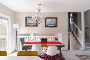 Un comedor con una mesa de madera, sillas blancas y amarillas, una araña y pinturas de veleros en la pared.