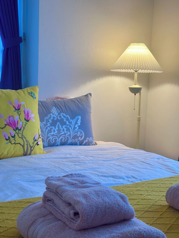 Una cama bien hecha con almohadas, una lámpara y toallas dobladas.