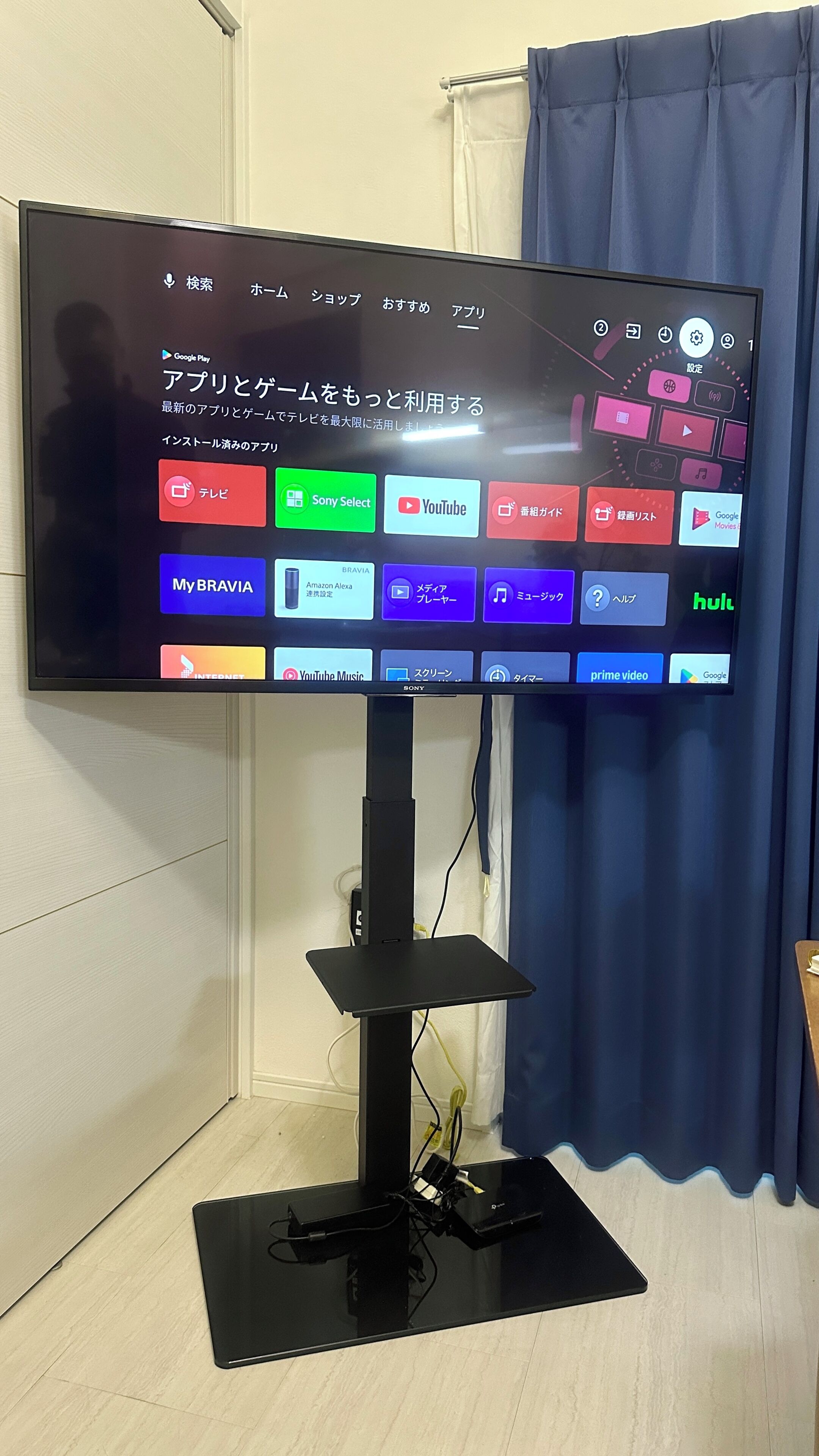 A flat-screen TV mounted on a stand with a remote control, displaying various streaming apps.