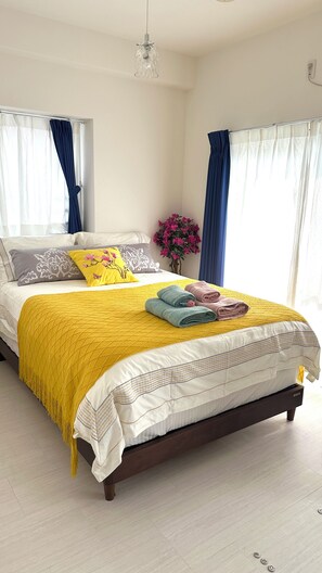 A neatly made bed with a yellow blanket, pillows, and folded towels. - SunSea Okinawa Stunning Ocean View 2BR Sleeps 6 20 min from Airport 3 min to Shopping Mall (Urasoe)