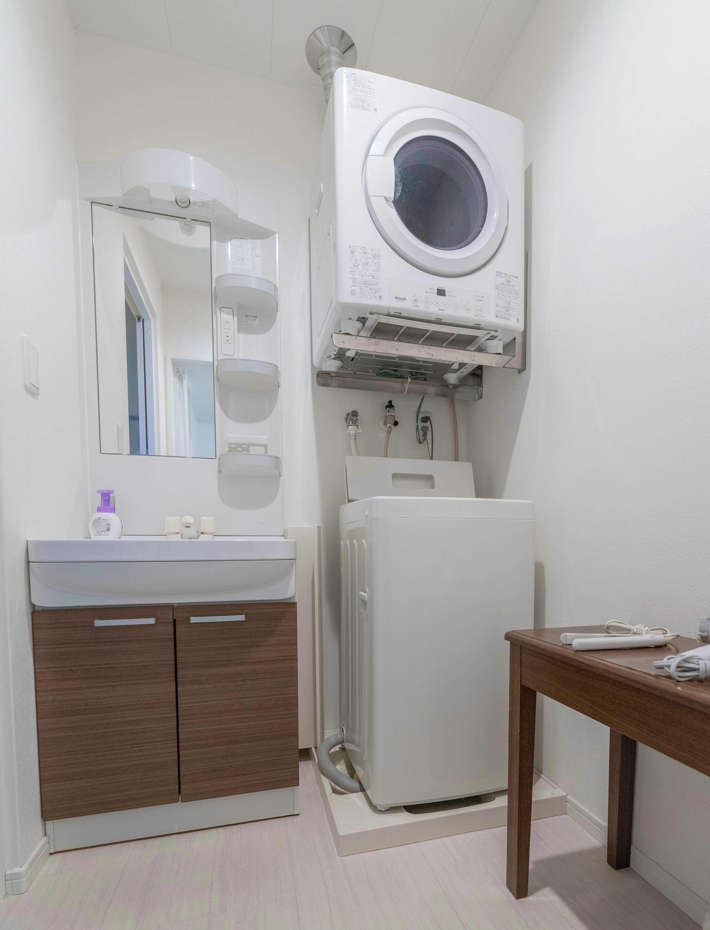 A compact bathroom with a built-in washer and dryer, a wooden vanity, and a mirror.