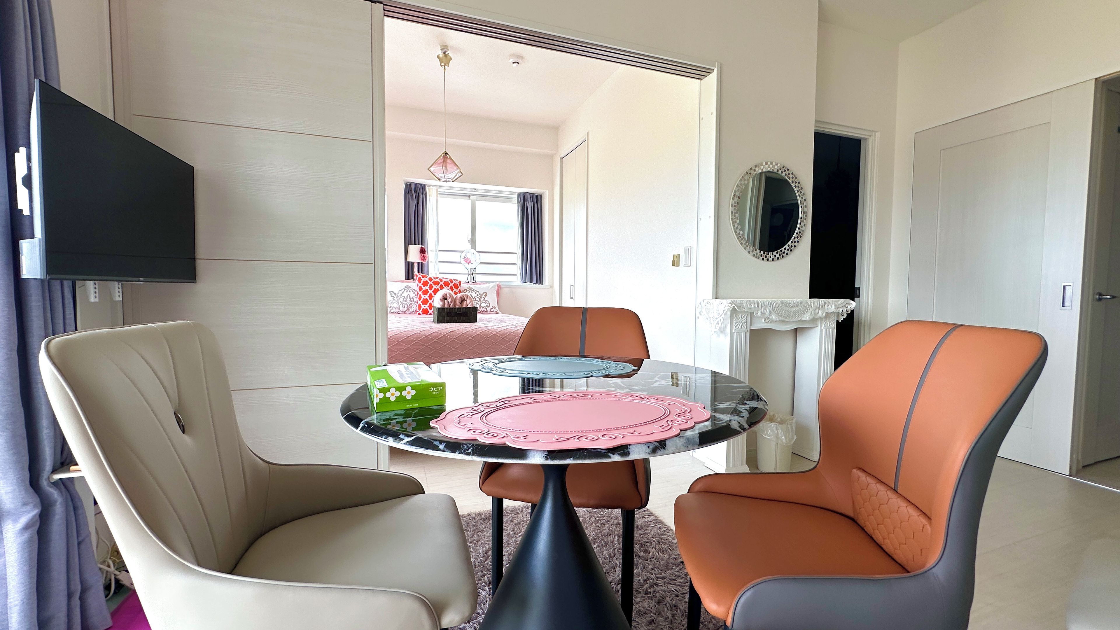 A hotel room with a dining area featuring a round table, two chairs, and a television mounted on the wall.