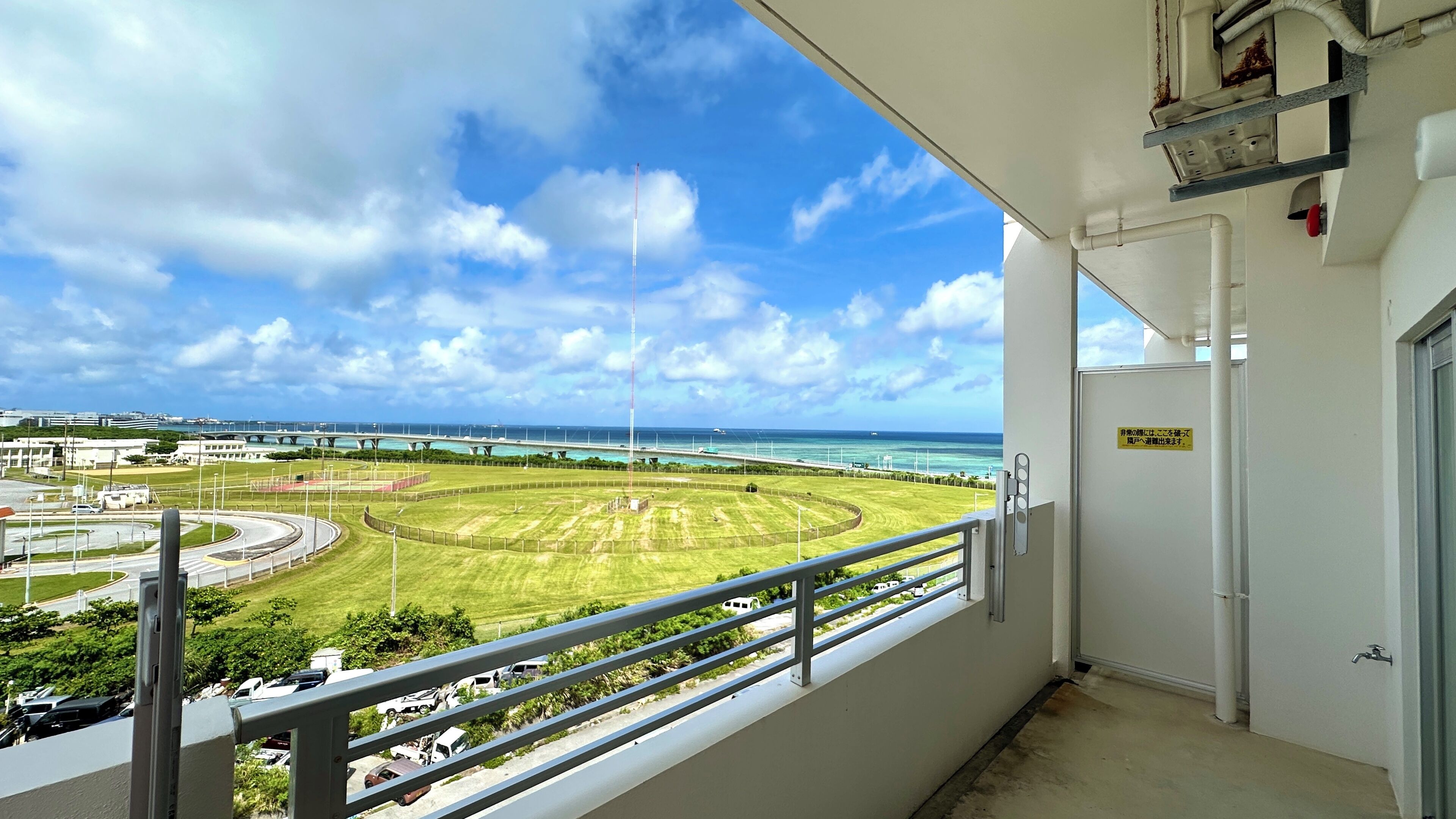 A balcony with a view of a coastal area, including a road, greenery, and a bridge.