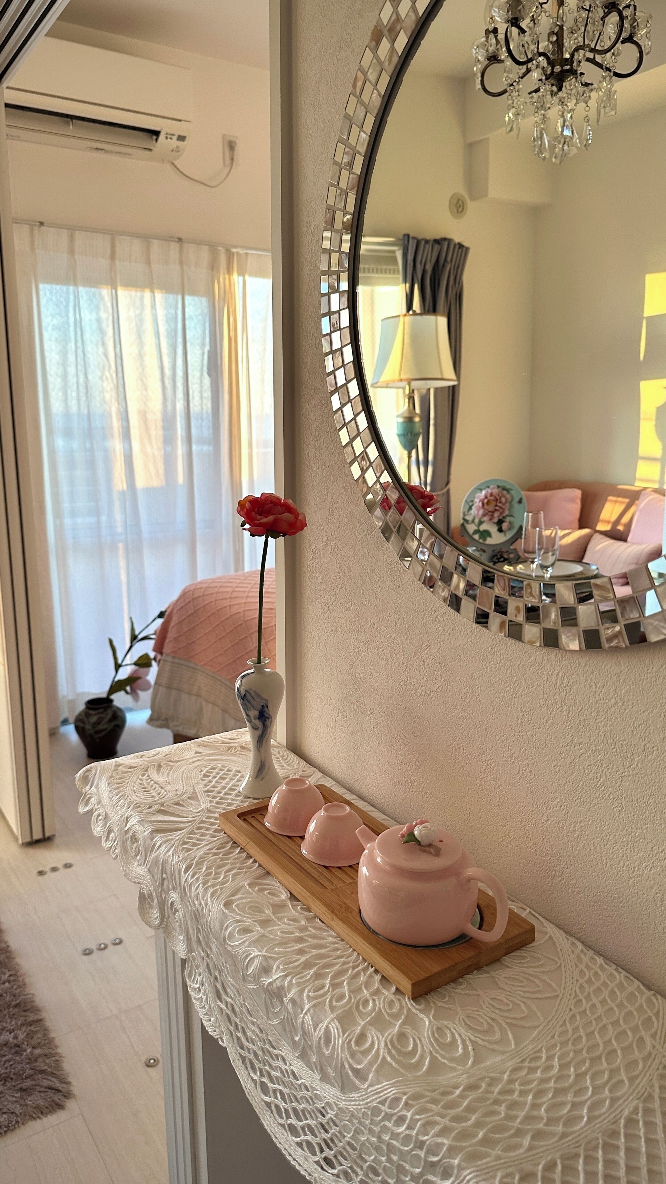 A room with a mirror, a vase with a single flower, and a tray with two teapots.