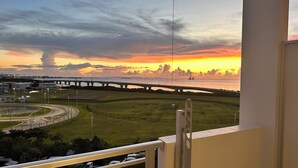 A view of a bridge over water during sunset, with a grassy area and a roundabout in the foreground. - SunSea Okinawa Stunning Ocean View 2BR Sleeps 6 20 min from Airport 3 min to Shopping Mall (Urasoe)
