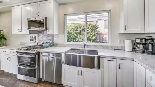 A modern kitchen with stainless steel appliances, white cabinetry, and a large window providing a view of the outdoors. - Pet-Friendly Home • Yard + Deck • Minutes to DT SD (Lemon Grove)