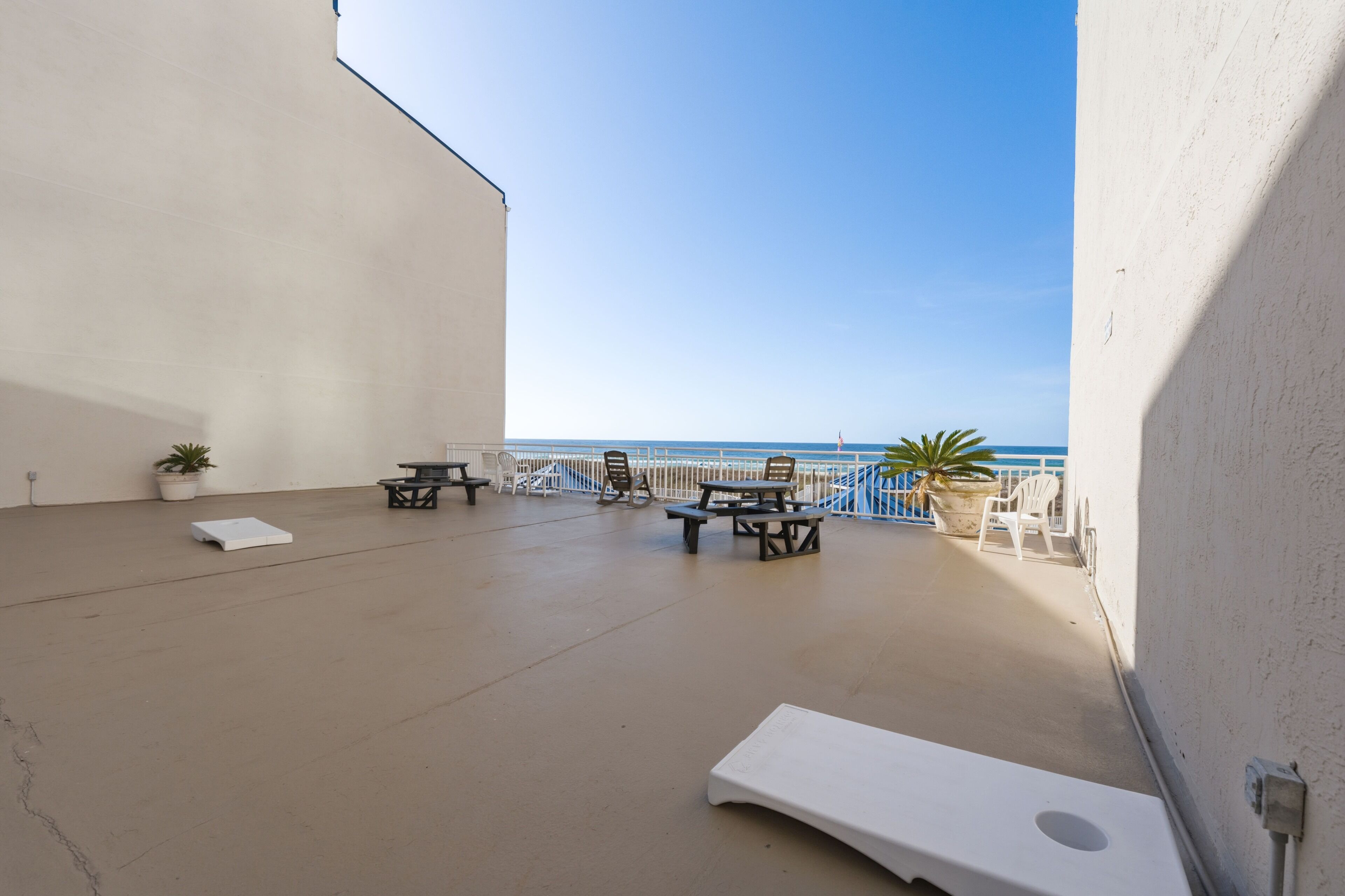 A balcony with a view of the sea, featuring a lounge chair, picnic tables, and potted plants.