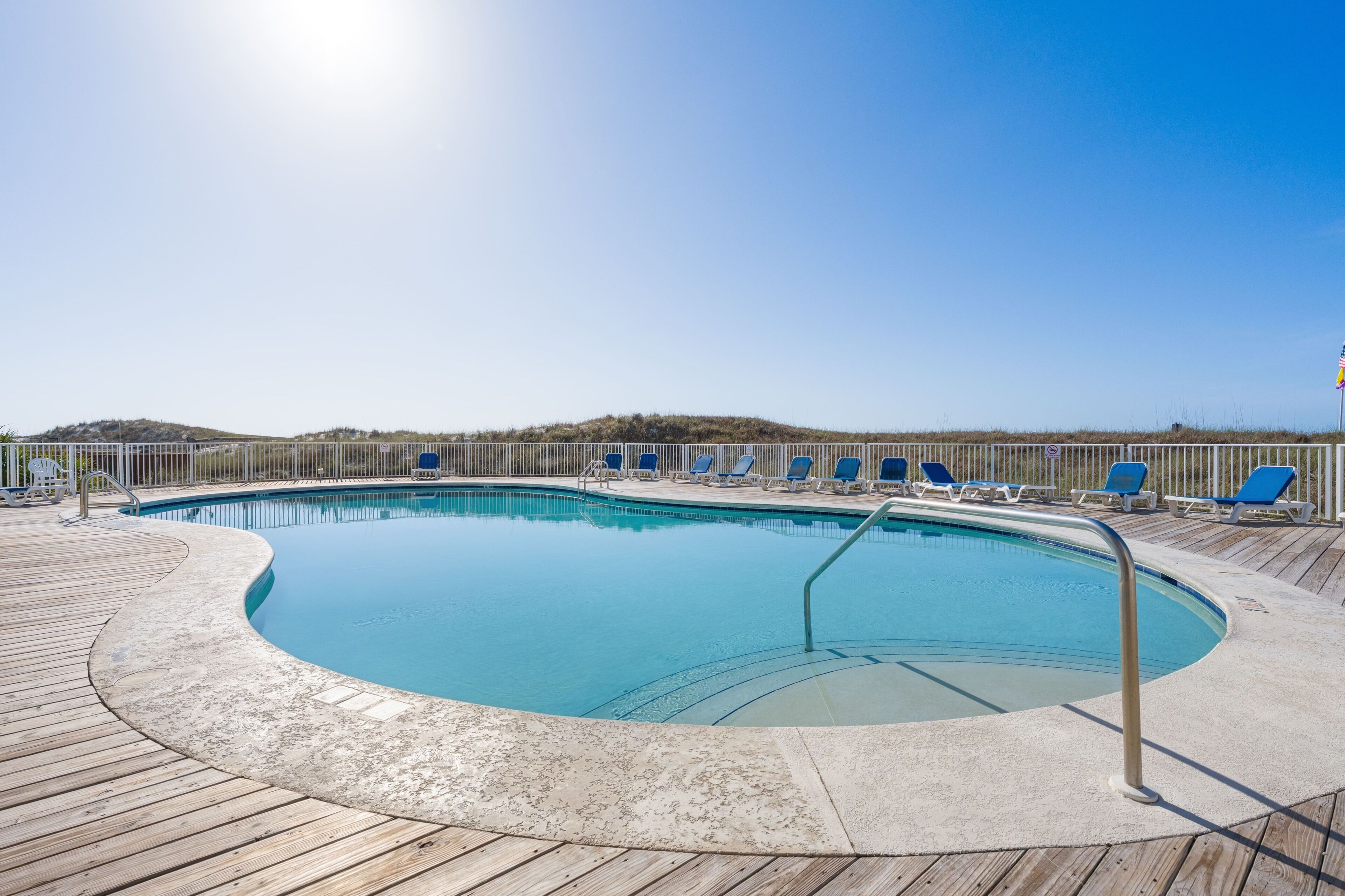 A swimming pool with a wooden deck, lounge chairs, and a flag.