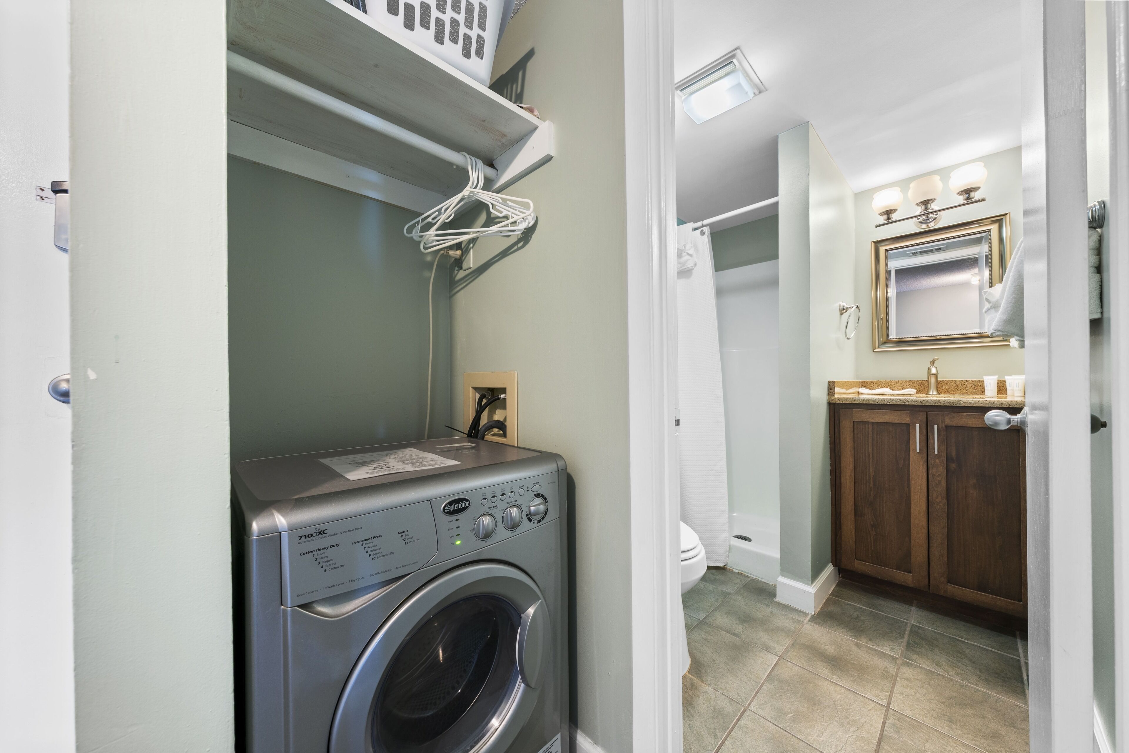 Une buanderie équipée d’un lave-linge à chargement frontal, d’un étendoir et d’un espace douche avec un meuble-lavabo et un miroir.