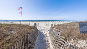 A sandy beach path leading to the ocean, with a flag and a sign indicating beach rules. - Sugar Beach 313 (Orange Beach)