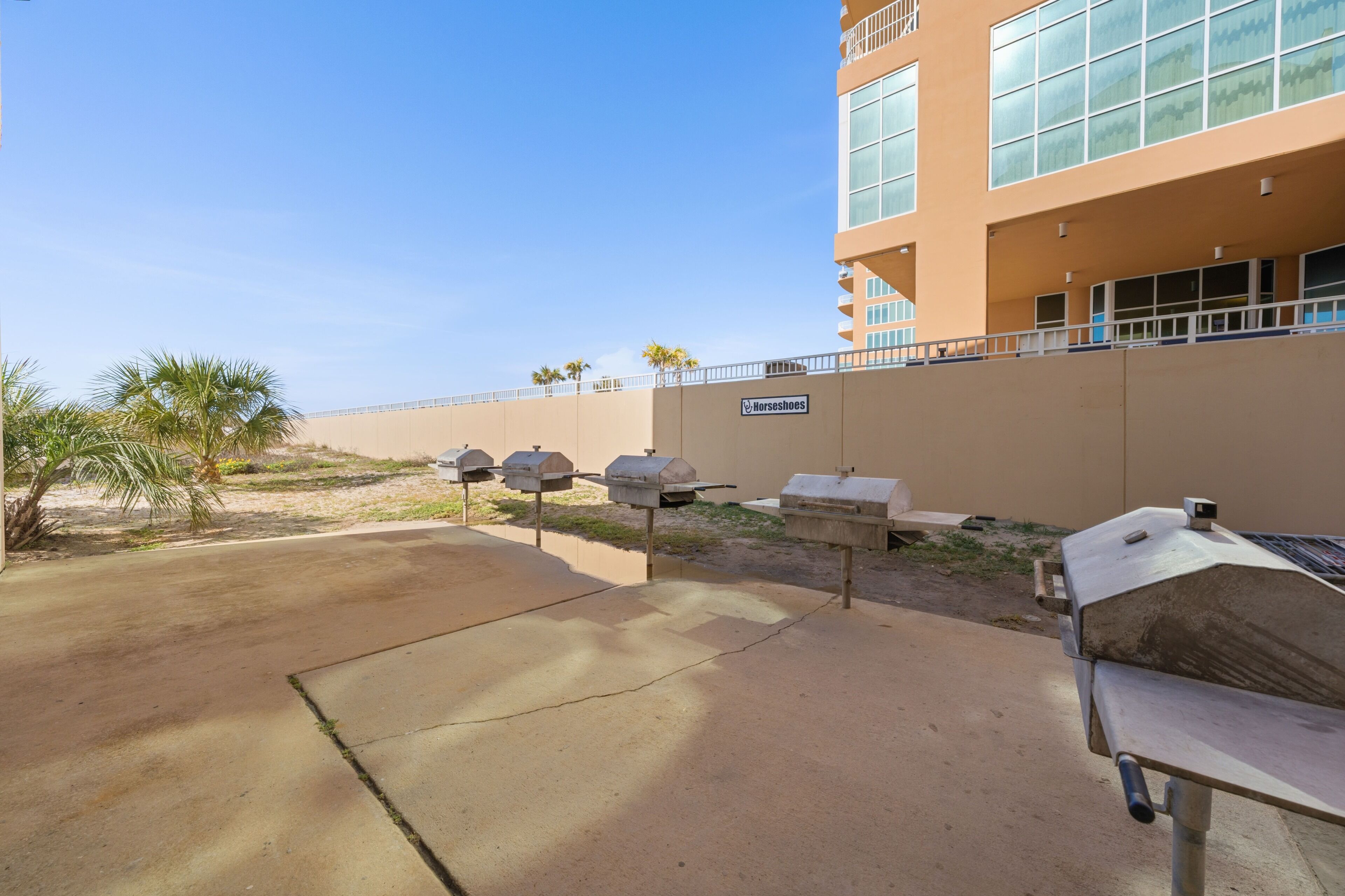 A concrete patio with outdoor grills and mailboxes, a building with large windows and a sign reading 'Norseshoes,' and a clear blue sky.