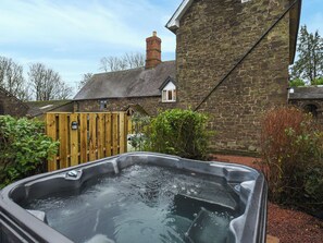 A hot tub in a garden with a stone building and wooden fence in the background. - 5 bedroom accommodation in Church Stretton (Church Stretton)