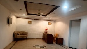 A hallway with a beige sofa, a small table with a red lamp, and a wooden cabinet. - Sapphire Lodge (Islamabad)