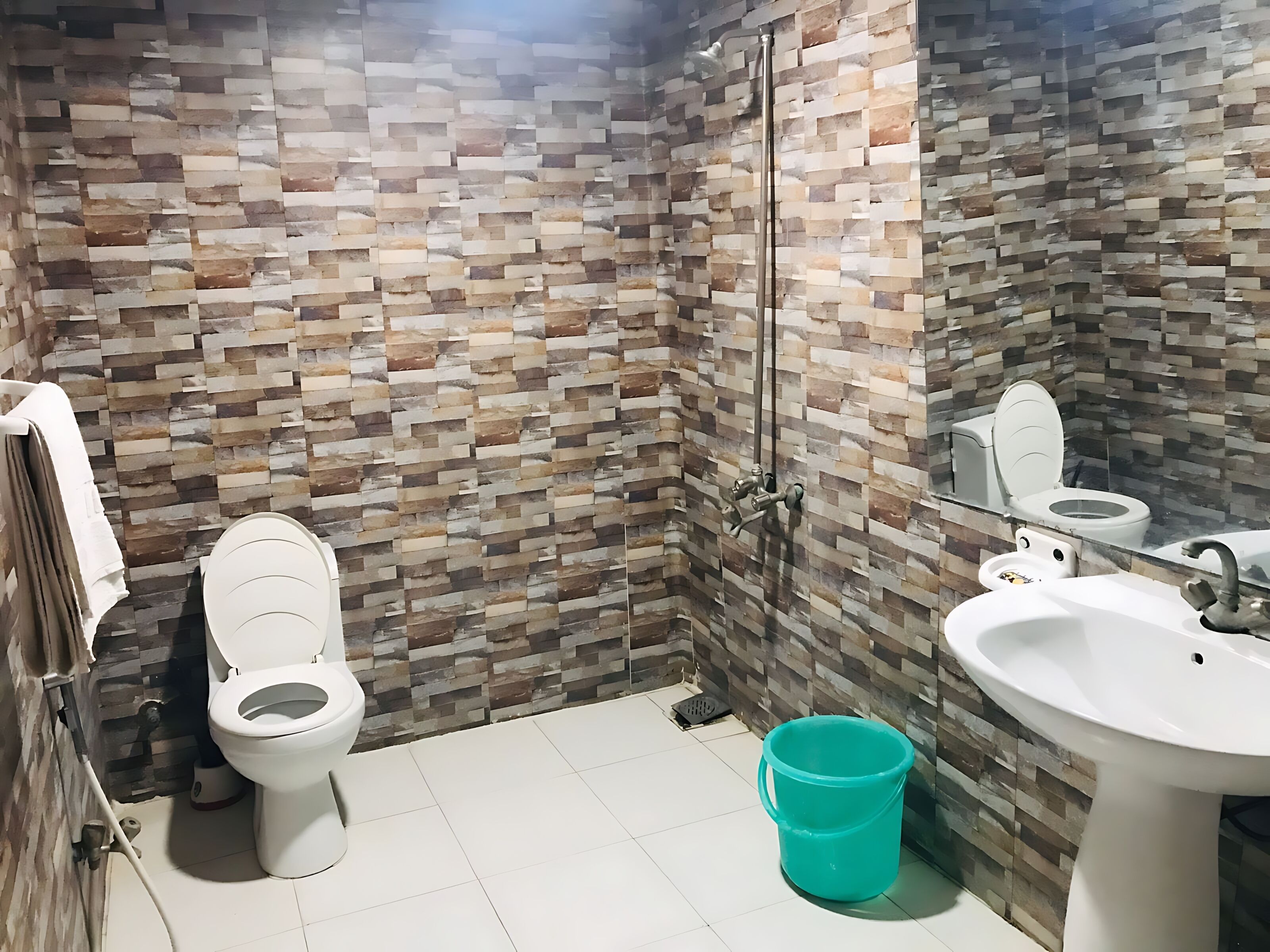 Une salle de bain avec un sol carrelé, des toilettes, un lavabo et un espace douche doté d’une porte en verre.
