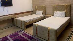 A hotel room with two single beds, a TV mounted on the wall, a small desk, and a purple patterned rug. - Sapphire Lodge (Islamabad)