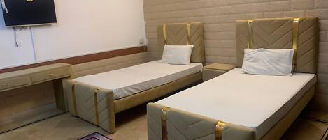 Habitación de hotel con dos camas individuales, un televisor en la pared, un escritorio pequeño y una alfombra morada estampada.