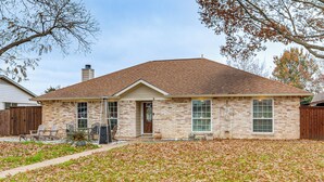 A two-story brick house with a brown roof, a front porch with chairs, and a yard covered in fallen leaves. - Dallas Area Home w/ Hot Tub, Families Welcome! (Duncanville)