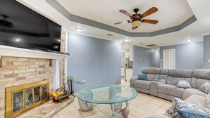 A living room with a fireplace, a glass-top coffee table, and a gray sectional sofa. - Dallas Area Home w/ Hot Tub, Families Welcome! (Duncanville)