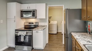 A compact kitchen with white cabinets, a built-in microwave, a stainless steel refrigerator, a stove, and a washing machine. - 2 Mi to Motor Speedway! Indy Home w/ Fenced Yard (Indianapolis)