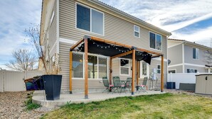 Une maison à deux étages dotée d’un patio couvert, d’un espace salon extérieur et d’une grande poubelle noire.